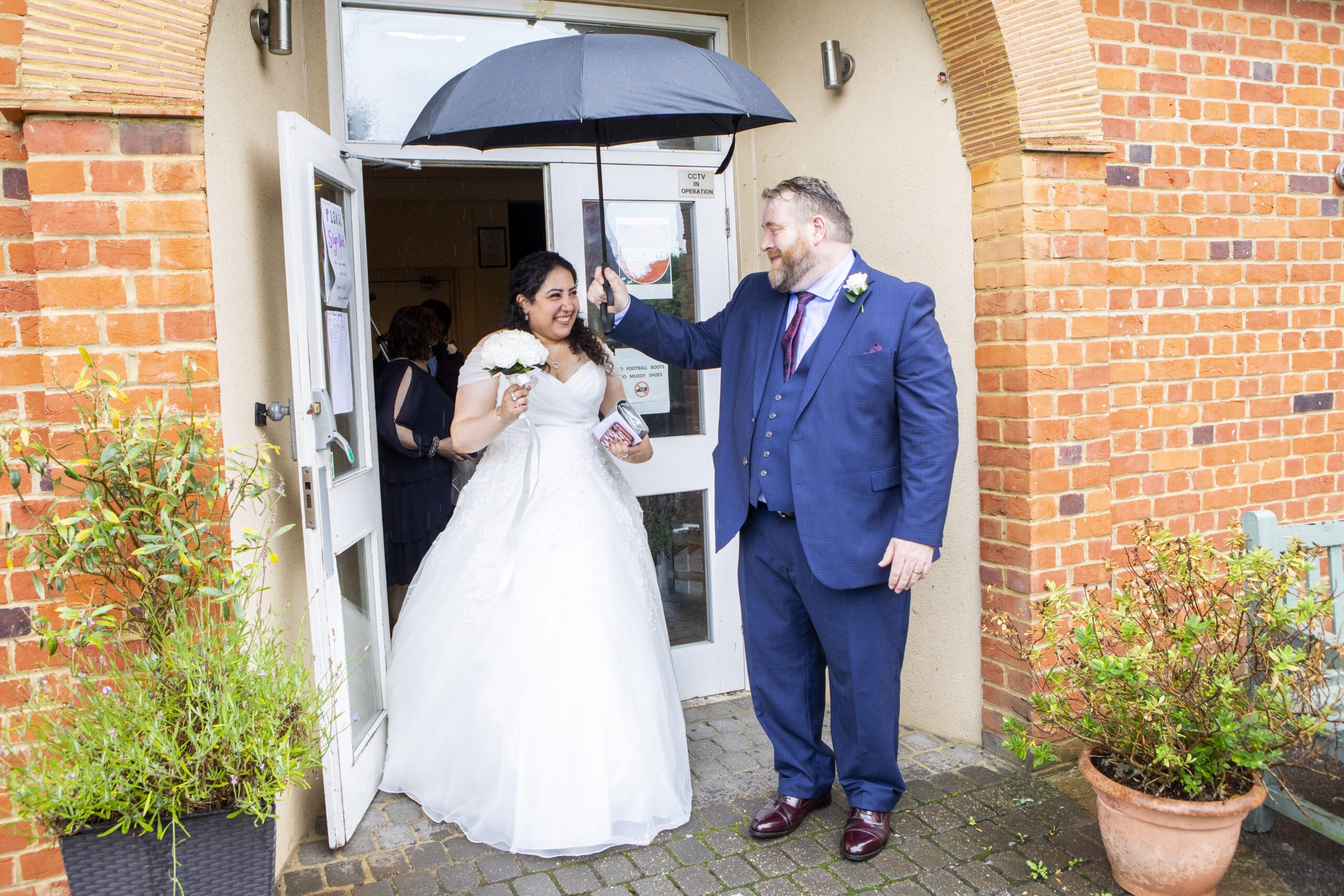 Wedding couple outside the Brentham Club in Ealing with the groom holding an umbrella